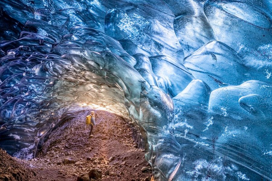 Female tourist admiring light shining through blue crystal ice cave