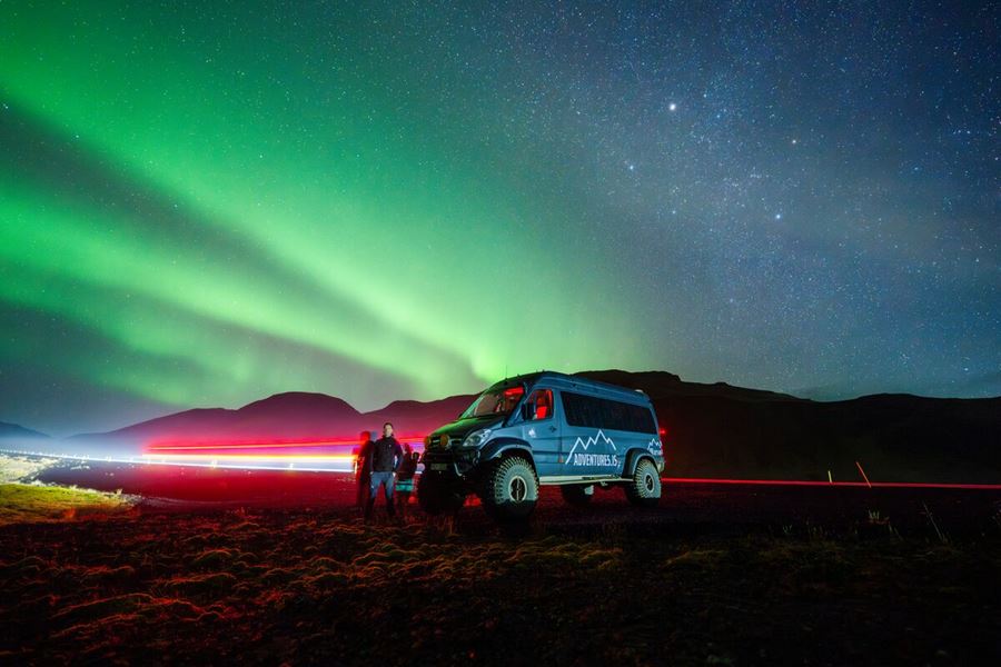 Bright super jeep lights shining red and green aurora borealis in the night sky on tour in Iceland.