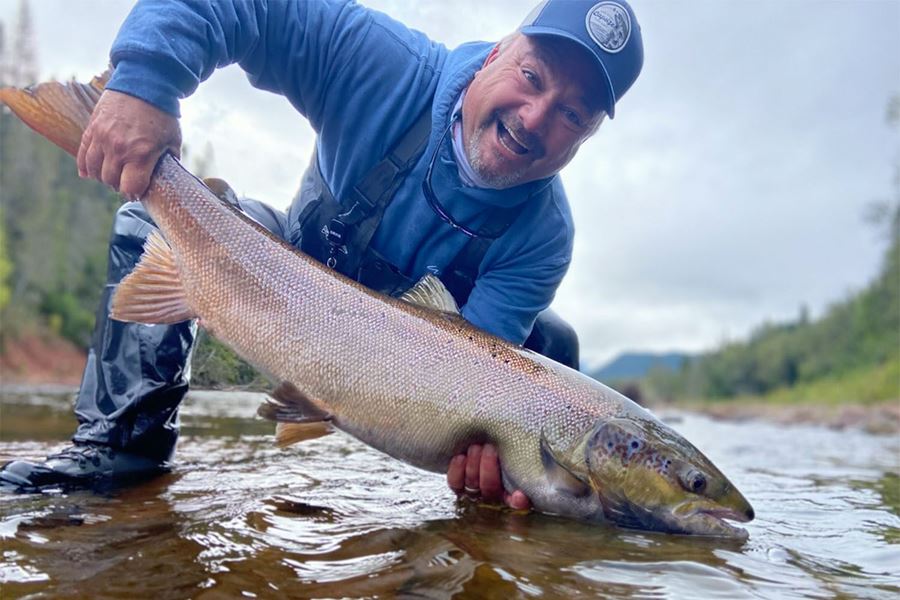Man with blue sweater and cap holding salmon in river