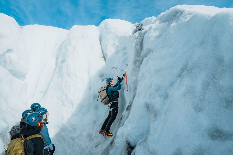 Glacier guide and tourist climbing glacier ice crevasse in Iceland,