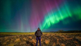 Male tourist posing underneath Aurora Borealis at lava field in South West Iceland.
