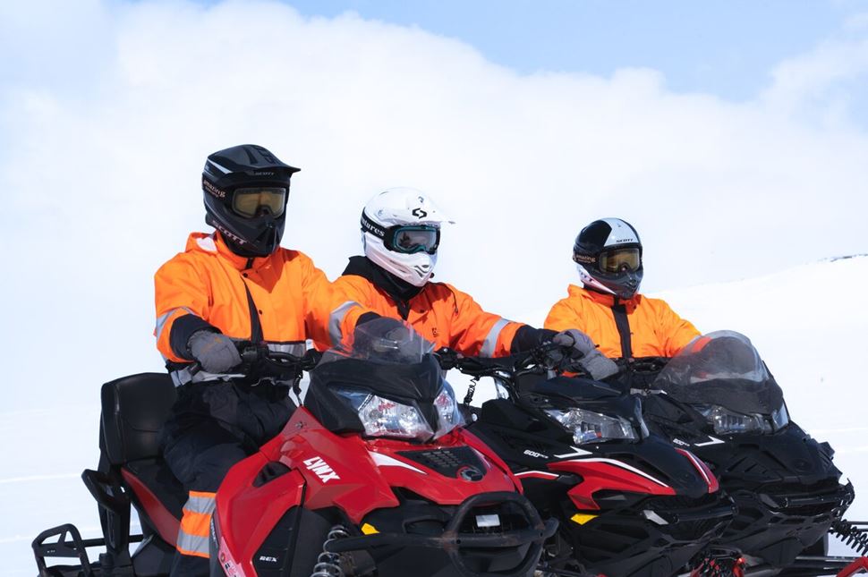 Close up view of three snowmobilers in orange gear on red snowmobiles 