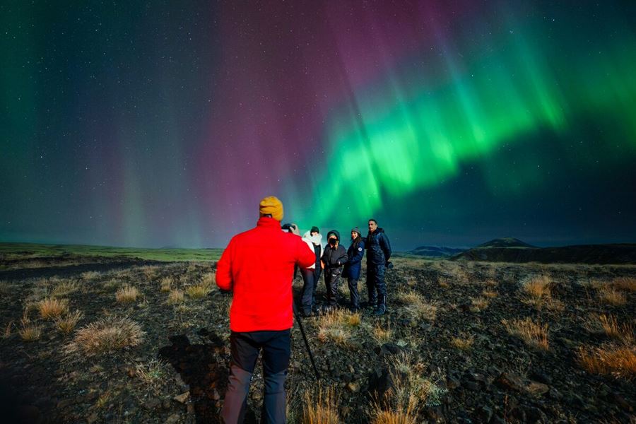 Tour guide photographing small group of tourists underneath the northern lights in Autumn in Iceland.