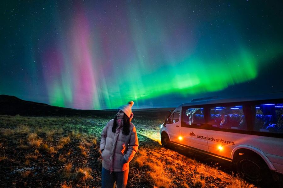 Female posing underneath bright show of northern lights in south west Iceland in autumn.