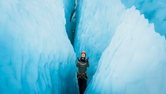 Tourist standing in between huge blue ice crevasse at Vatnajokull.
