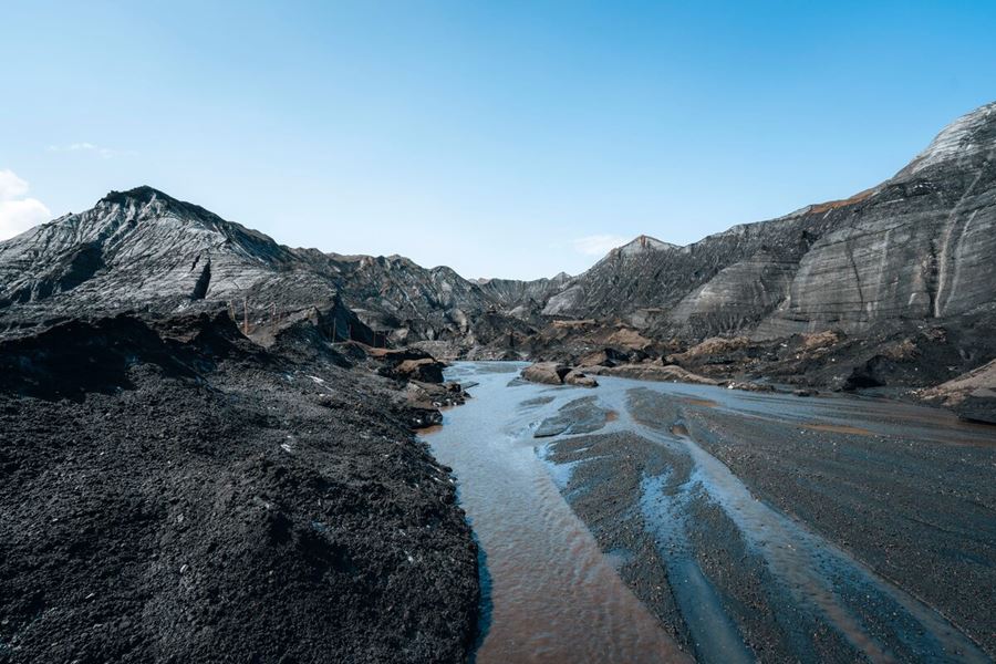Scenic view of the Katla Volcano surroundings with winding glacial streams cutting through black volcanic sand and moss-covered terrain under a cloudy sky in Iceland.