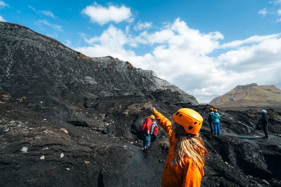 Hikers walking along a rugged trail near the Katla Volcano, surrounded by volcanic landscapes, moss-covered lava fields and blue skies.