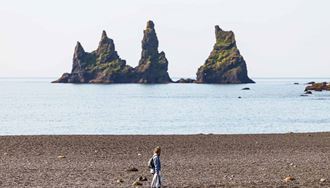 woman walking close to reynisdrangar in reynisfjara