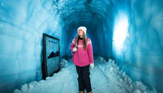 Female tourist in pink sweater walking through blue ice tunnel at Langjokull