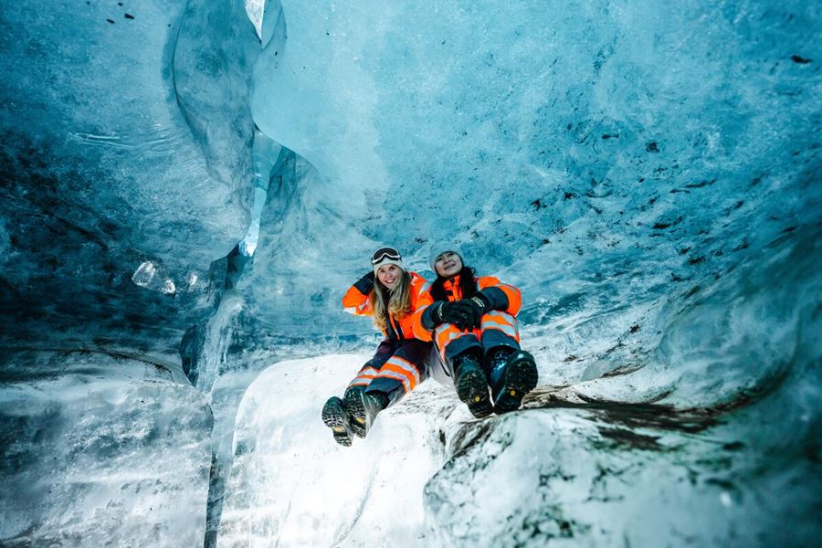 Two Women Sitting Inside Of An Ice Cave In Iceland