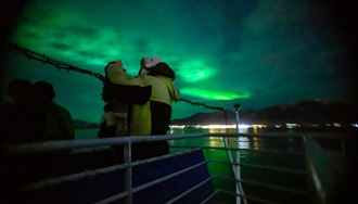 Tourist on Northern lights boat tour standing on edge of boat viewing the sky 