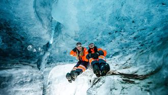 Two Women Sitting Inside Of An Ice Cave In Iceland