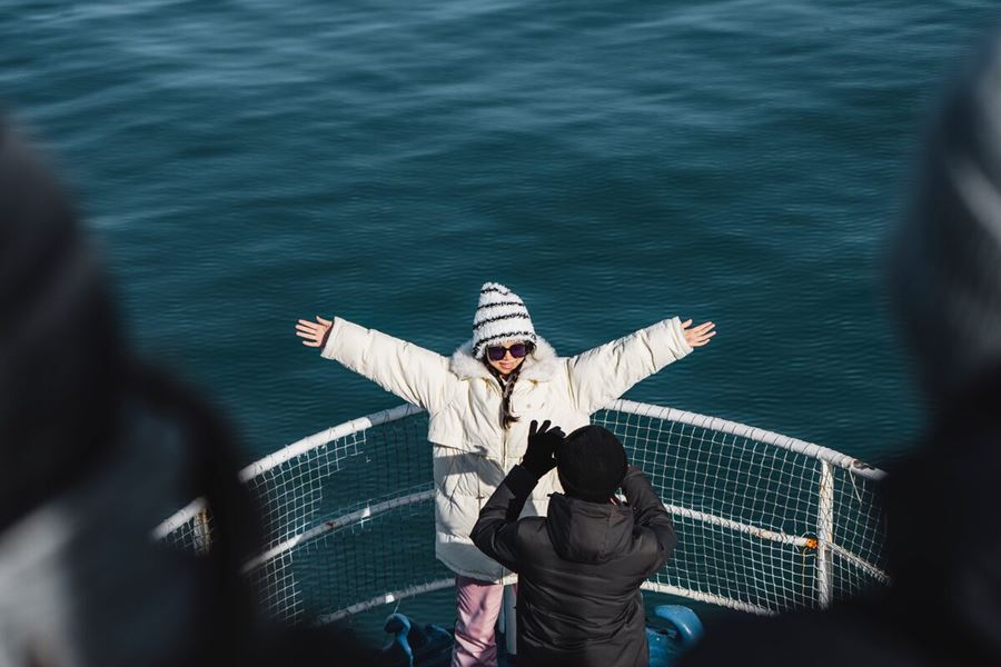 Female dressed in white coat with arms up in air posing for photo on boat.
