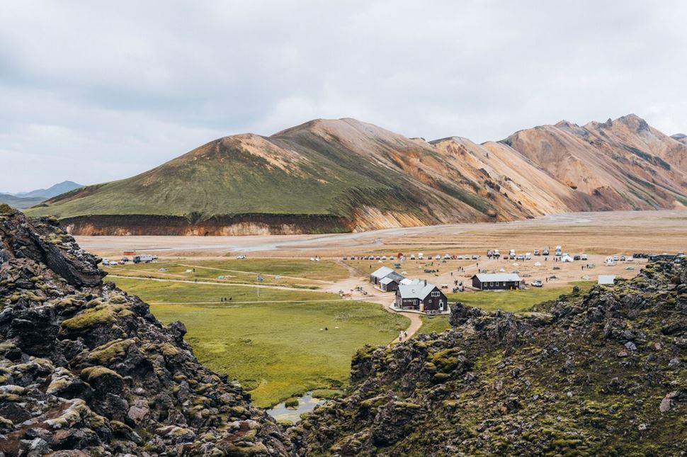 Hiking huts and people  in distance in field in front of different colored mountains 
