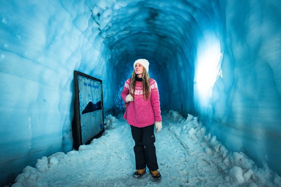 Female tourist in pink sweater walking through blue ice tunnel at Langjokull