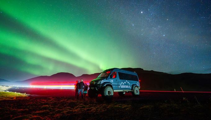 Bright super jeep lights shining red and green aurora borealis in the night sky on tour in Iceland.
