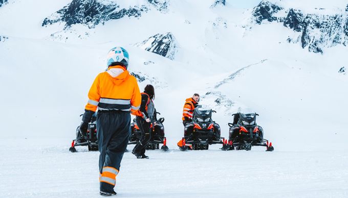 Small tour wearing orange safety gear snowmobiling together in front of Langjokull glacier.
