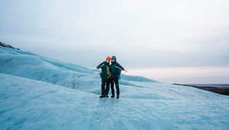 Couple posing for photo standing on blue glacier floor holding ice picks