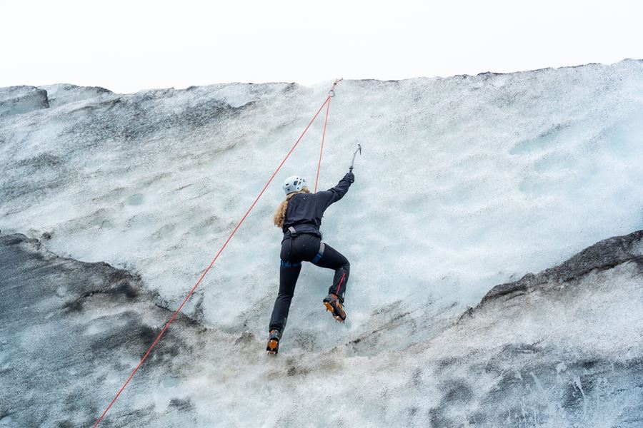 Female suspended with orange rope climbing ice wall at Sólheimajökull in safety gear and crampons 