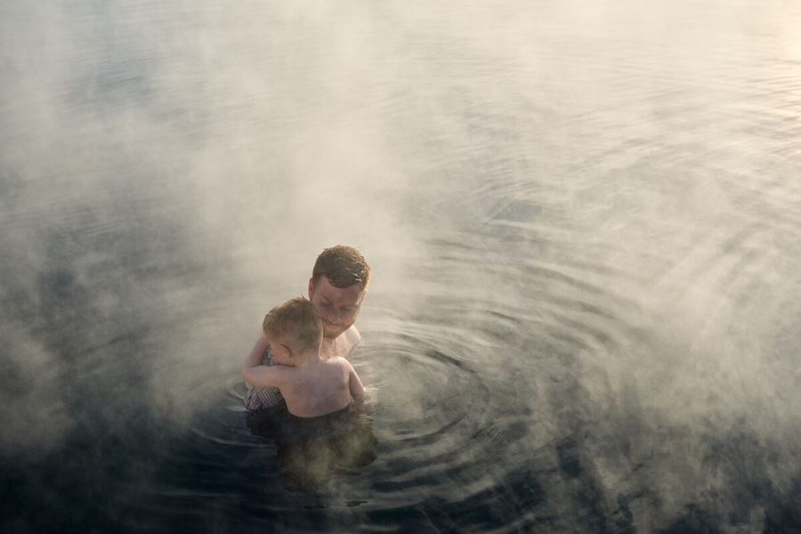 Sun down reflecting on geothermal pool with father and child bathing