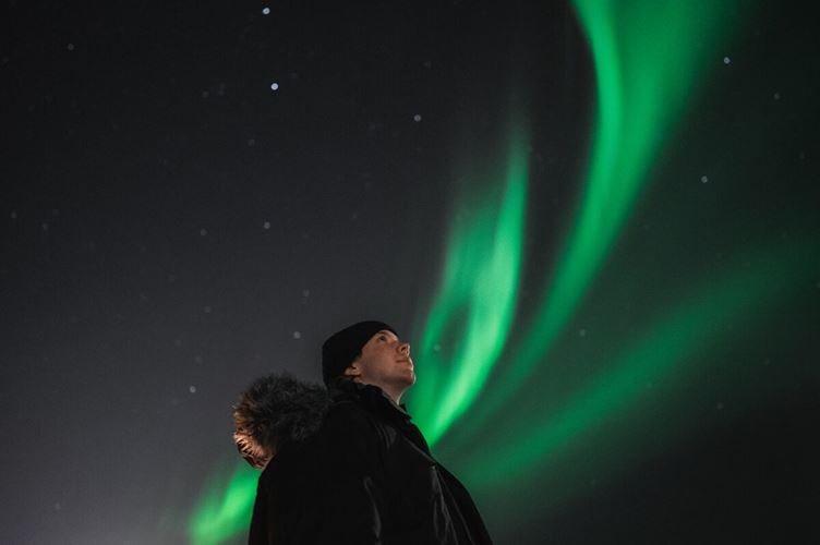 Close up of male in a beanie hat staring up to northern lights night sky 