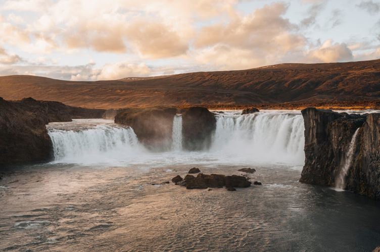 Trio of waterfalls cascading into river by bed of autumn covered land  